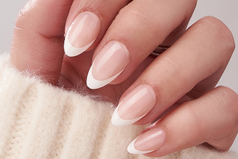 A hand with soft almond French-tip nails resting on a cream knit sweater.