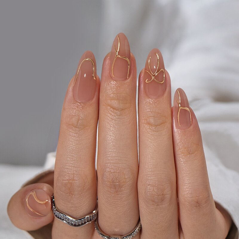  A hand wearing two rings showing almond-shaped, nude, press-on nails with a custom gold chrome design.