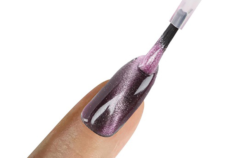 A close-up of deep plum magnetic cat eye polish being applied to a nail with a brush.