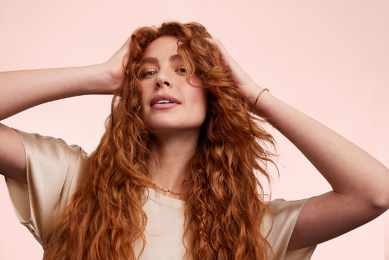 A woman with long copper red waves running her hands through her hair.
