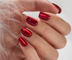 A hand with glossy red cat eye nail polish resting against white feathers.