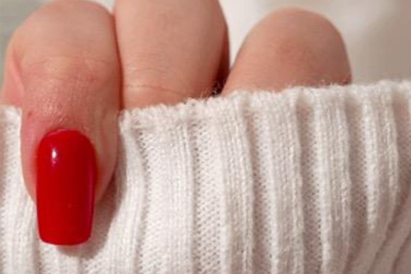 A hand with a glossy red square manicure peeking out of a white sweater cuff.