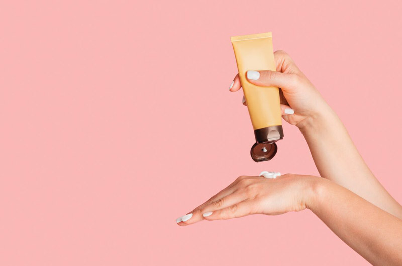 hands applying moisterizer with pink background