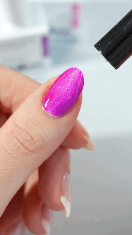 A woman's hand with pink cat eye nail polish on the thumb, using a cat eye magnet to create the effect.
