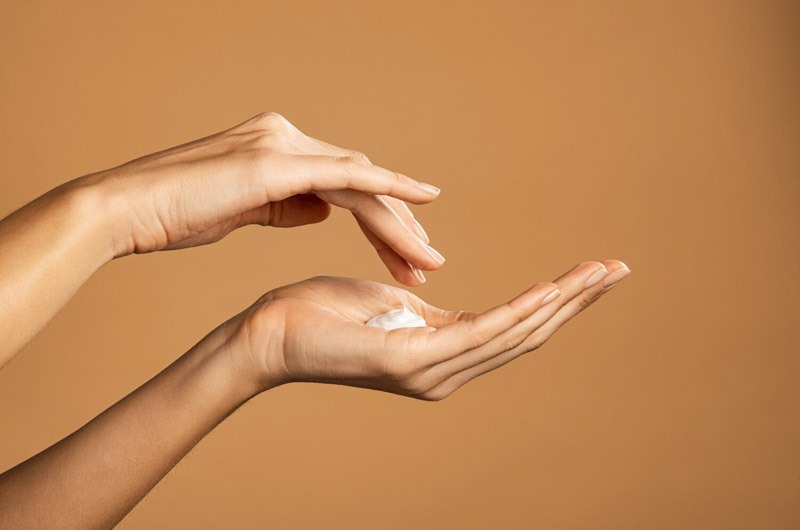hands applying lotion with brown background